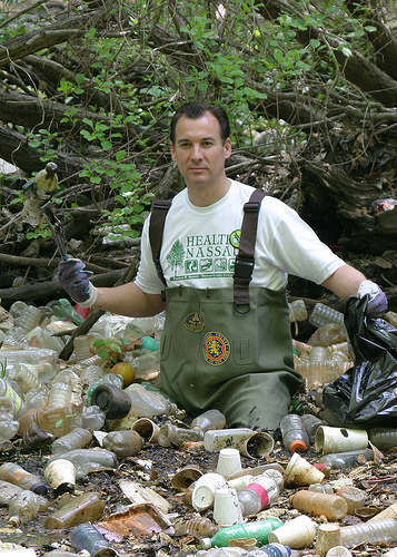 In chest-high waders and rubber gloves, Tom Suozzi stands in the midst of floating bottles, placing them in plastic bags